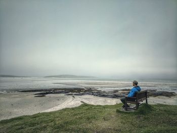 Man sitting on seat at beach against sky