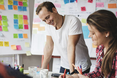 Smiling businessman standing by female colleague working on table