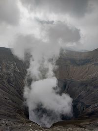 Smoke emitting from volcanic landscape against sky