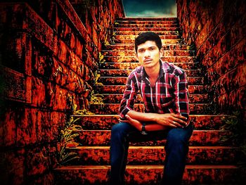 Portrait of young man sitting against wall