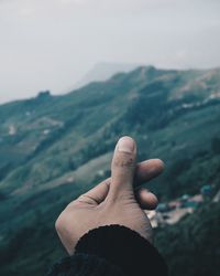 Person hand on mountain against sky