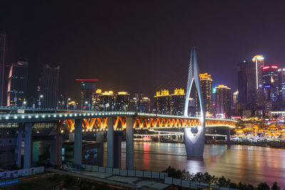 Illuminated bridge over river against buildings at night