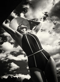 A portrait of a woman in a swimsuit, hat and sunglasses in summer on the riverbank against the sky