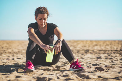 Full length of woman sitting on beach against sky