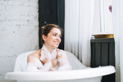 Young happy woman taking bath with foam at home, treat yourself