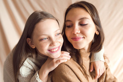 Sisters hugging on beige color textile background