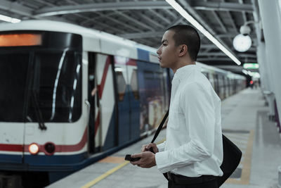 Side view of man standing by train at railroad station