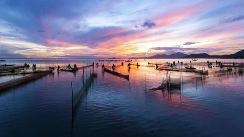 Wooden posts in sea at sunset