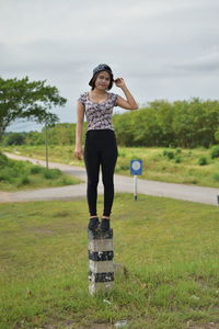 Portrait of young woman standing on bollard against cloudy sky