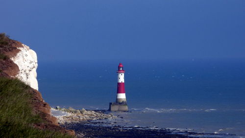 Lighthouse at sea shore against clear blue sky