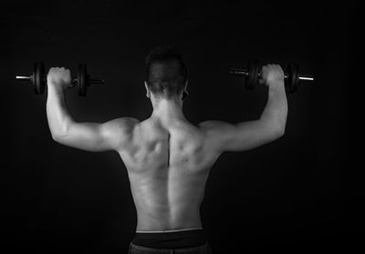 Rear view of shirtless man looking at camera over black background