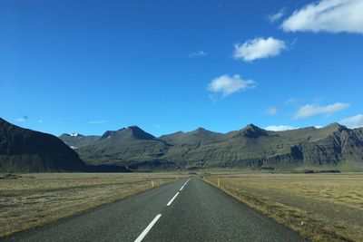 Road leading towards mountains against blue sky
