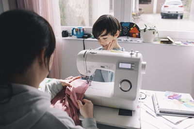 Son looking at mother sewing clothes at home
