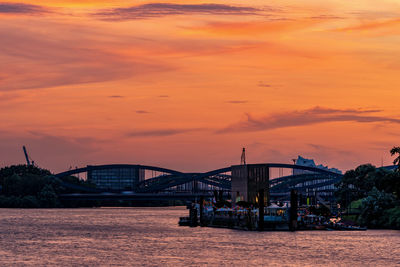 Bridge over river against dramatic sky during sunset