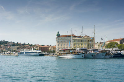 Sailboats in sea by buildings against sky
