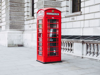 Red telephone booth on sidewalk against building in city