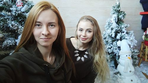 Portrait of beautiful woman with female friend against christmas decorations