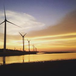 Low angle view of wind turbine and lake at sunset