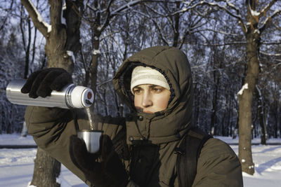 Man drinks hot tea from metal thermos. leisure activity in winter forest at sunset.