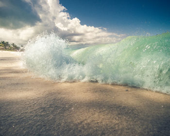Waves breaking on beach against sky