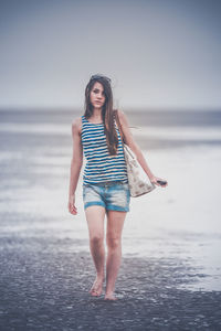 Full length portrait of young woman walking at beach