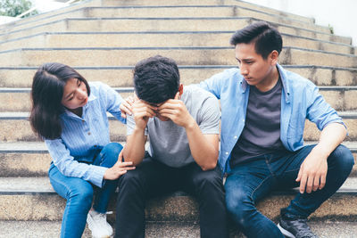 Friends looking at tensed friend while sitting on steps