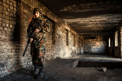 Young soldiers with guns, a soldier in equipment and with arms inspects a ruined house outside the