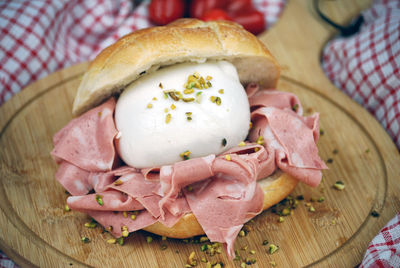 Sandwich with mozzarella, mortadella and chopped pistachios on a wooden cutting board