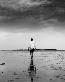 Rear view of man standing on beach against sky