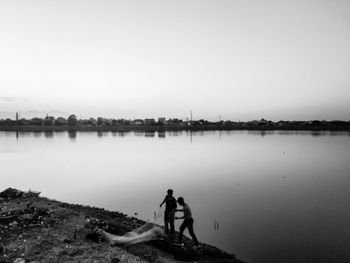 Men standing on lake against sky