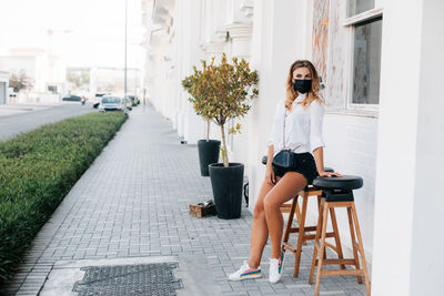 A young woman wearing a protective mask waits for her order while sitting on a chair