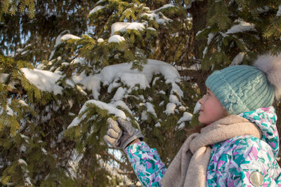 Side view of girl standing by snow covered tree in forest