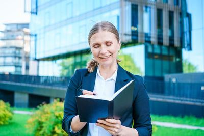 Successful beautiful business woman standing against backdrop buildings writes