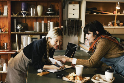 Multiracial female coworkers discussing over diary at upcycling workshop