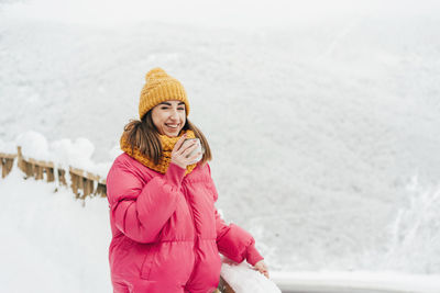 Happy woman in a landscape of winter snowy mountains laughs and drinks tea.