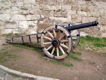 Old fashioned wheel on field against brick wall