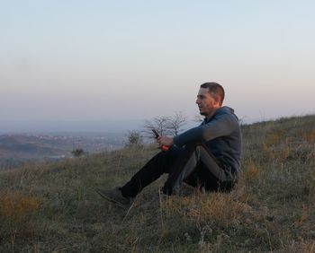 Man sitting on field against sky during sunset