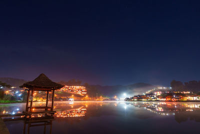 Illuminated buildings by river against sky at night