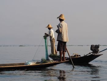 Rear view of people standing on boat in sea against sky