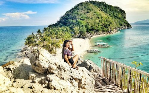 Woman sitting on rock by sea against sky