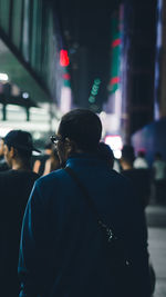 Rear view of man standing on illuminated street at night