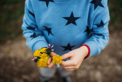 Close up of boy holding yellow flowers outside on a cold day in spring