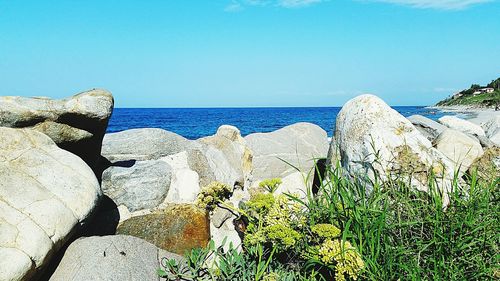 Scenic view of rocks by sea against blue sky