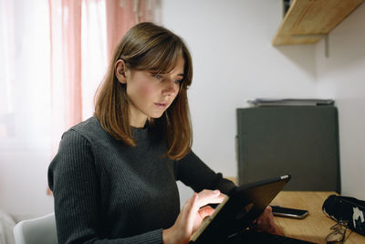 Blonde girl sitting at a desk at home looking at a tablet