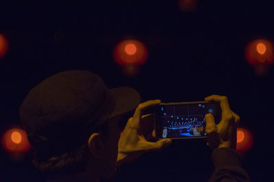 Man photographing illuminated lights through mobile phone at night