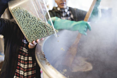 Woman pouring ingredients in container while assisting coworker at brewery