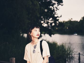 Portrait of woman standing by lake against trees