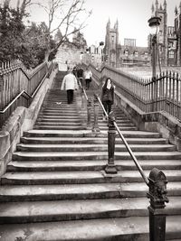 Staircase by footbridge in city against sky