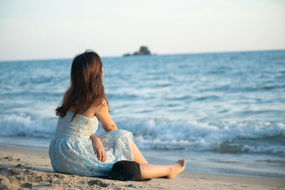 Woman sitting at beach against sky