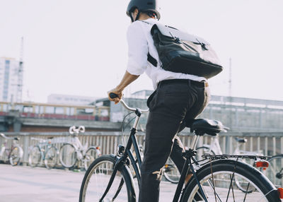 Rear view of businessman with backpack riding bicycle on sidewalk in city